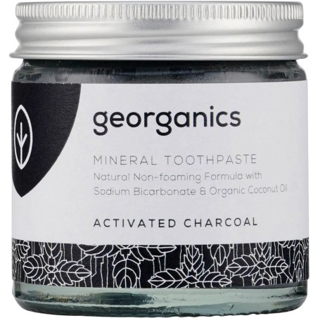 Frasco de vidrio con dentífrico de crema de coco y carbón activo de Georganics para un blanqueamiento dental natural.