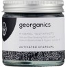 Frasco de vidrio con dentífrico de crema de coco y carbón activo de Georganics para un blanqueamiento dental natural.